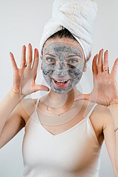 beautiful girl in towel applying black caly mask on face isolated on white gray