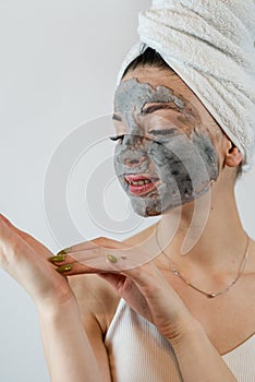 beautiful girl in towel applying black caly mask on face isolated on white gray