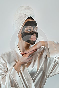 beautiful girl in towel applying black caly mask on face  on white gray