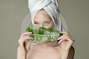 A beautiful girl with towel on her head holds a green leaf in her hands. Cleanliness and care