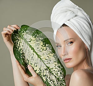 A beautiful girl with towel on her head holds a green leaf in her hands. Cleanliness and care