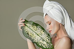 A beautiful girl with towel on her head holds a green leaf in her hands. Cleanliness and care