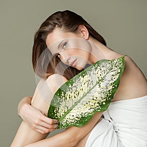 A beautiful girl with towel on her head holds a green leaf in her hands. Cleanliness and care