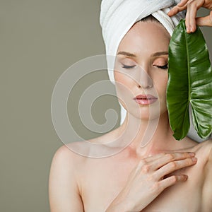 Beautiful girl with towel on her head holds a green leaf in her hands. Cleanliness and care