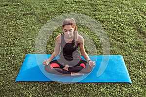 Beautiful girl training in city, meditating while sitting yoga mat. Fitness training active lifestyle. Tanned athletic