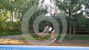 A beautiful girl training his legs with a chair and rubber stretch against a background of coniferous trees, slow motion