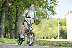 Beautiful girl traveling on electric bike, active young woman riding bicycle, female biking in park, in nature at summer