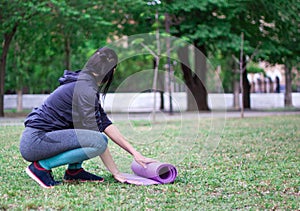 Beautiful    girl untwists the mat and preparing for  gymnastics and stretching  in the park.  Concept of sport