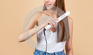 Beautiful girl using styler on her shining hair. Hairstyle. Beautiful smiling woman ironing long hair with flat iron