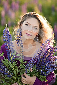 Beautiful girl in violet dress holding a lupine at sunset on the field. The concept of nature and romance
