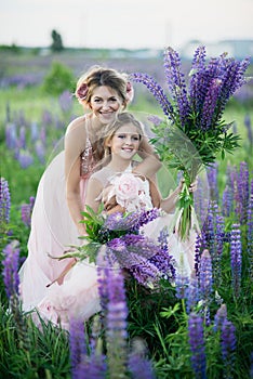 Beautiful girl in violet dress holding a lupine at sunset on the field. The concept of nature and romance