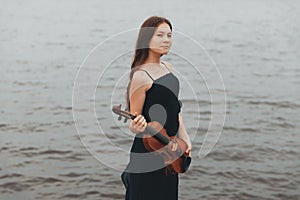 a beautiful girl with a violin stands against the background of water. Asian appearance. musical concept