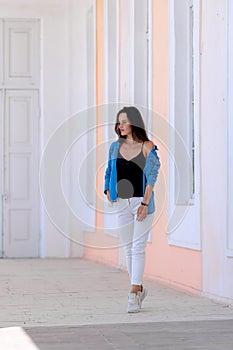 Beautiful girl walking in light hall with high celling. Girt in white jeans and blue shirt. Full length photo.