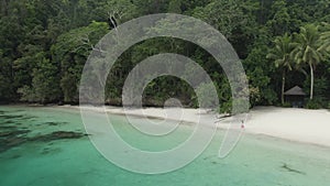 Beautiful Girl Walking On Ocean Beach With Huts Among Palm Trees In Triton Bay, Raja Ampat. Stunning View From Drone