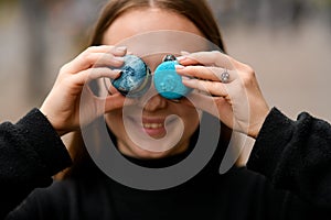 Beautiful girl wear in black keeps two sweet french macaroons on eyes