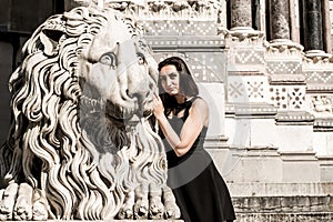 Beautiful girl wearing a black dress next to Gothic style lion statue