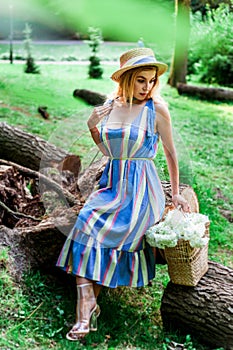 Beautiful girl wearing blue dress and hat collect flowers in basket in the wood.