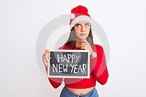 Beautiful girl wearing Christmas Santa hat holding blackboard over isolated white background serious face thinking about question,