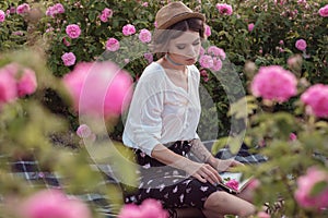 Beautiful girl wearing hat with book sitting on grass in rose gaden