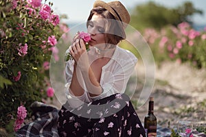 Beautiful girl wearing hat with book sitting on grass in rose gaden