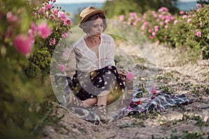 Beautiful girl wearing hat with book sitting on grass in rose gaden