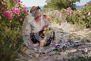 Beautiful girl wearing hat with book sitting on grass in rose gaden