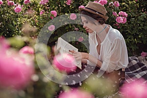 Beautiful girl wearing hat with book sitting on grass in rose gaden