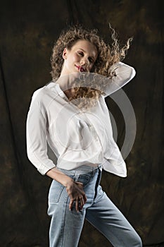 A beautiful girl, wearing jeans and a blouse, poses cheerfully in the wind, which blows her long curly hair and clothes.