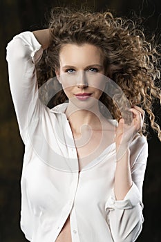 A beautiful girl, wearing jeans and a blouse, poses cheerfully in the wind, which blows her long curly hair and clothes. Close up