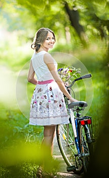 Beautiful girl wearing a nice white dress having fun in park with bicycle. Healthy outdoor lifestyle concept. Vintage scenery