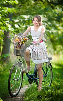 Beautiful girl wearing a nice white dress having fun in park with bicycle. Healthy outdoor lifestyle concept. Vintage scenery