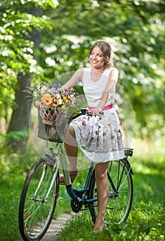 Beautiful girl wearing a nice white dress having fun in park with bicycle. Healthy outdoor lifestyle concept. Vintage scenery