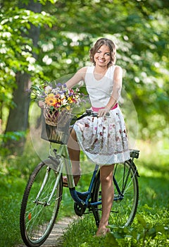 Beautiful girl wearing a nice white dress having fun in park with bicycle. Healthy outdoor lifestyle concept. Vintage scenery