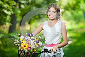 Beautiful girl wearing a nice white dress having fun in park with bicycle. Healthy outdoor lifestyle concept. Vintage scenery