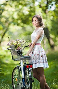 Beautiful girl wearing a nice white dress having fun in park with bicycle. Healthy outdoor lifestyle concept. Vintage scenery