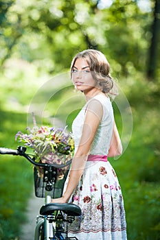 Beautiful girl wearing a nice white dress having fun in park with bicycle. Healthy outdoor lifestyle concept. Vintage scenery