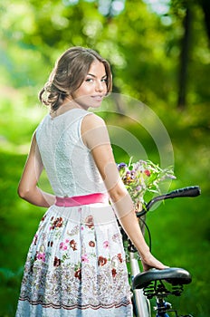 Beautiful girl wearing a nice white dress having fun in park with bicycle. Healthy outdoor lifestyle concept. Vintage scenery