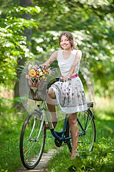 Beautiful girl wearing a nice white dress having fun in park with bicycle. Healthy outdoor lifestyle concept. Vintage scenery