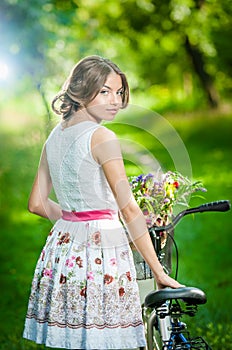 Beautiful girl wearing a nice white dress having fun in park with bicycle. Healthy outdoor lifestyle concept. Vintage scenery