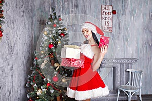 Beautiful girl wearing santa claus clothes . Smiling woman with big and small gift. Women on dress and santa`s hat.