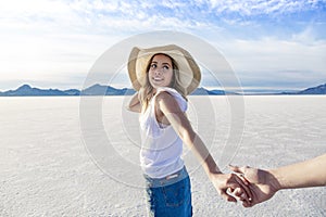 Beautiful girl wearing a sun hat holding her boyfriend`s hand and looking back at him