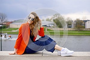 Beautiful girl wearing sunglasses at riverside. Girl sitting on pier and lookingat the river. Beautiful young girls outdoors