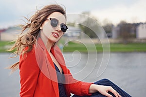 Beautiful girl wearing sunglasses at riverside. Girl sitting on pier and lookingat the river. Beautiful young girls outdoors