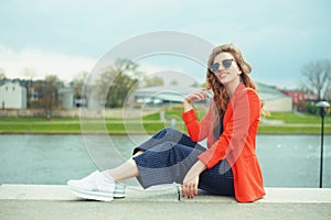 Beautiful girl wearing sunglasses at riverside. Girl sitting on pier and lookingat the river. Beautiful young girls outdoors in
