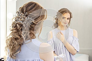 Beautiful girl with a wedding hairstyle looks at herself in the mirror, portrait of a young girl. beautiful make-up.