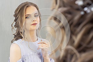 Beautiful girl with a wedding hairstyle looks at herself in the mirror, portrait of a young girl. beautiful make-up.