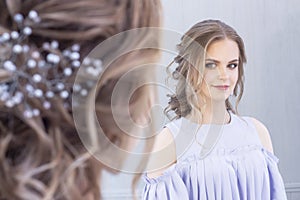 Beautiful girl with a wedding hairstyle looks at herself in the mirror, portrait of a young girl. beautiful make-up.