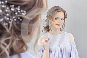 Beautiful girl with a wedding hairstyle looks at herself in the mirror, portrait of a young girl. beautiful make-up.