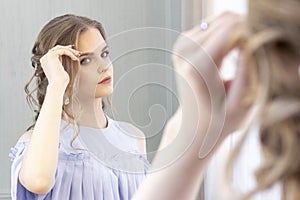 Beautiful girl with a wedding hairstyle looks at herself in the mirror, portrait of a young girl. beautiful make-up.