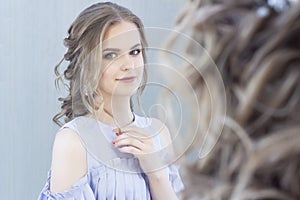 Beautiful girl with a wedding hairstyle looks at herself in the mirror, portrait of a young girl. beautiful make-up.